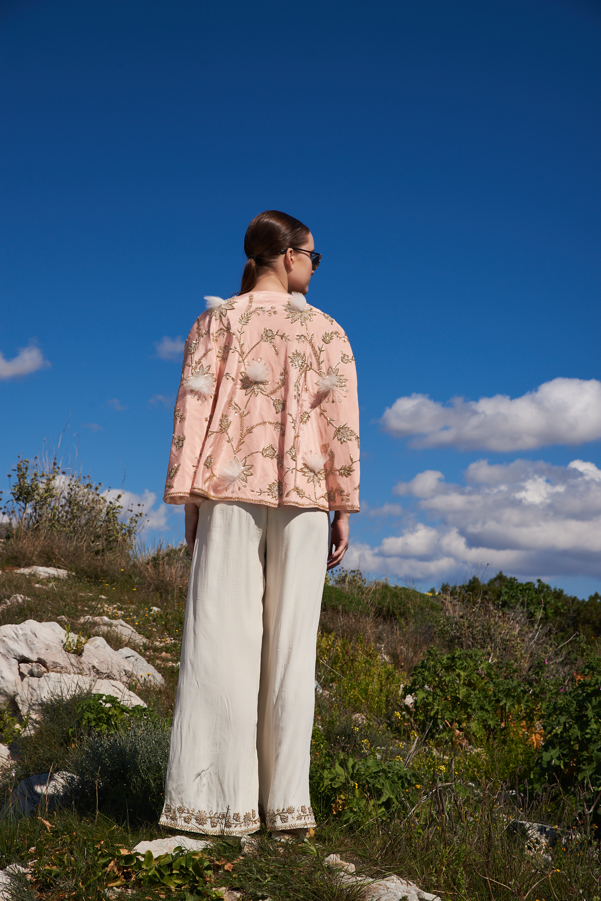 Salmon embroidered cape with feathers and white jumpsuit with embroidery at hem